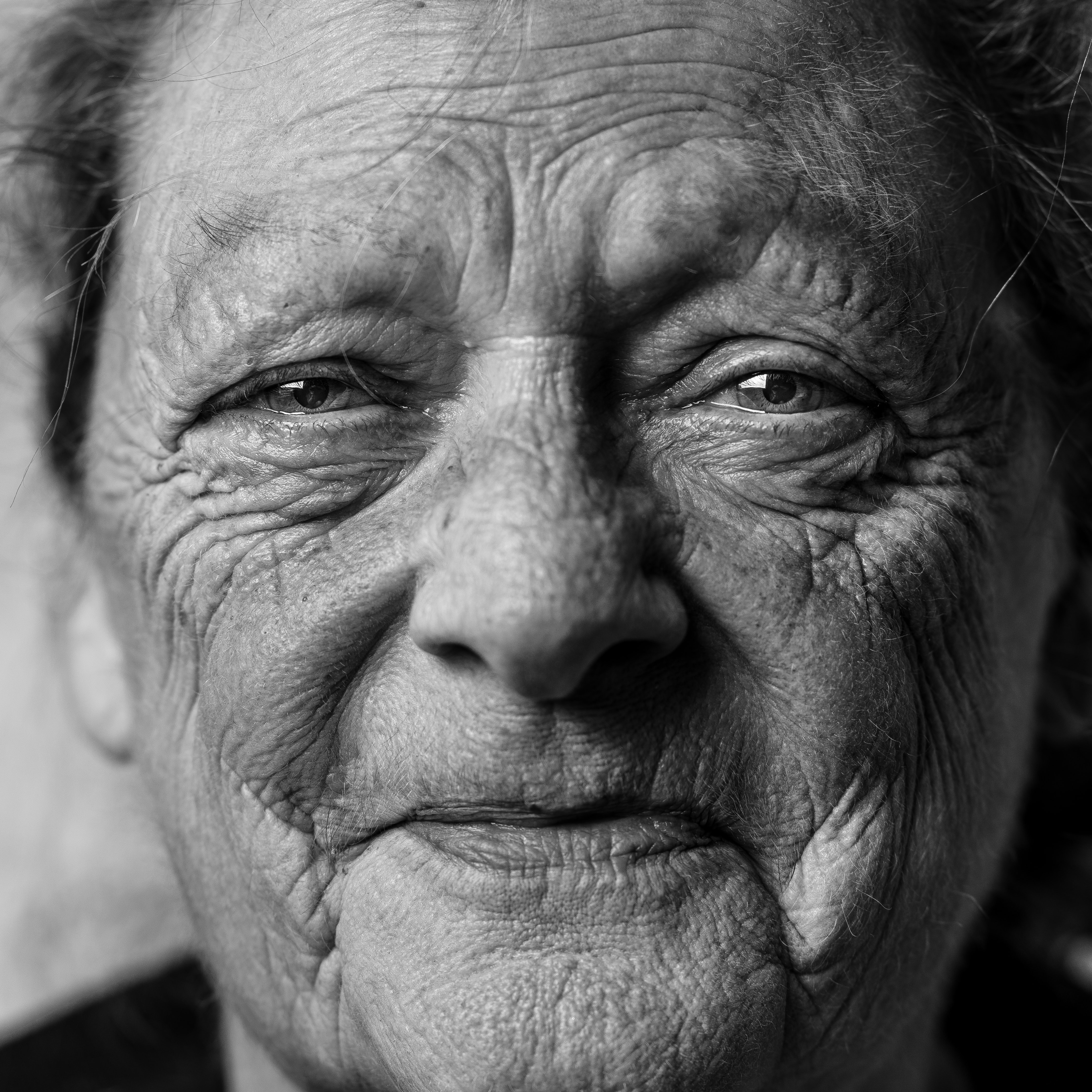 A smiling elderly woman, her face adorned with a multitude of wrinkles, gazes at the camera, conveying a sense of reassurance that all will be well.